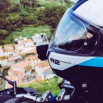 Casque intégral moto Schuberth blanc et bleu en gros plan, avec une vue plongeante sur un village de montagne en arrière-plan