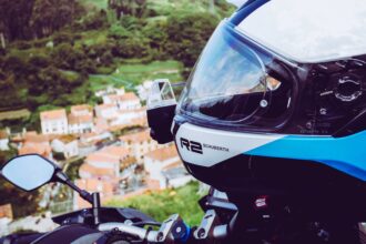 Casque intégral moto Schuberth blanc et bleu en gros plan, avec une vue plongeante sur un village de montagne en arrière-plan