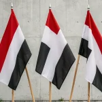 Trois drapeaux aux couleurs rouge blanc noir et noir blanc rouge accrochés côte à côte sur des mâts en bois, illustrant les différences entre ces drapeaux nationaux