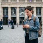Jeune femme avec smartphone devant gare européenne