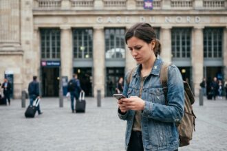 Jeune femme avec smartphone devant gare européenne