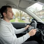 Homme au volant d'une voiture garée, adoptant une attitude calme et réfléchie avant de prendre la route