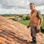 Couvreur professionnel debout sur un toit en tuiles de terre cuite en Vendée, vue grand angle sur la campagne environnante