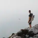 man in black jacket and brown shorts standing on rock during daytime