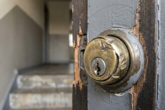 Gros plan sur une serrure de porte d'appartement forcée après un cambriolage, métal rayé et bois éclaté autour de la gâche